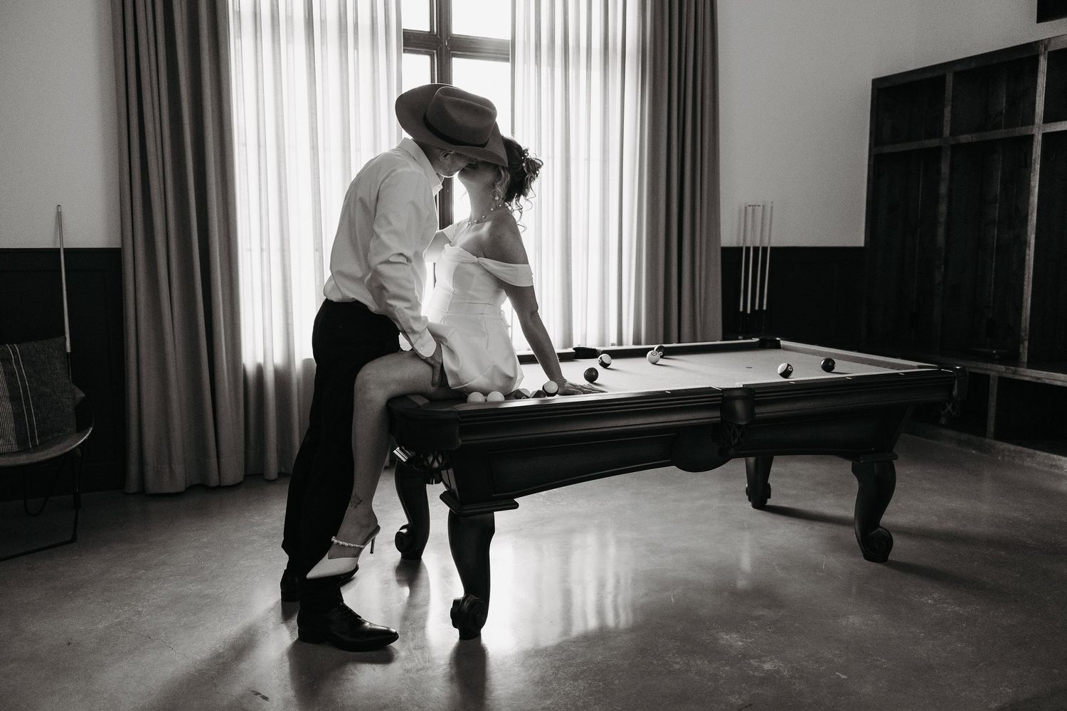 Romantic couple sharing an intimate moment on a pool table in a stylish room, black and white photography.