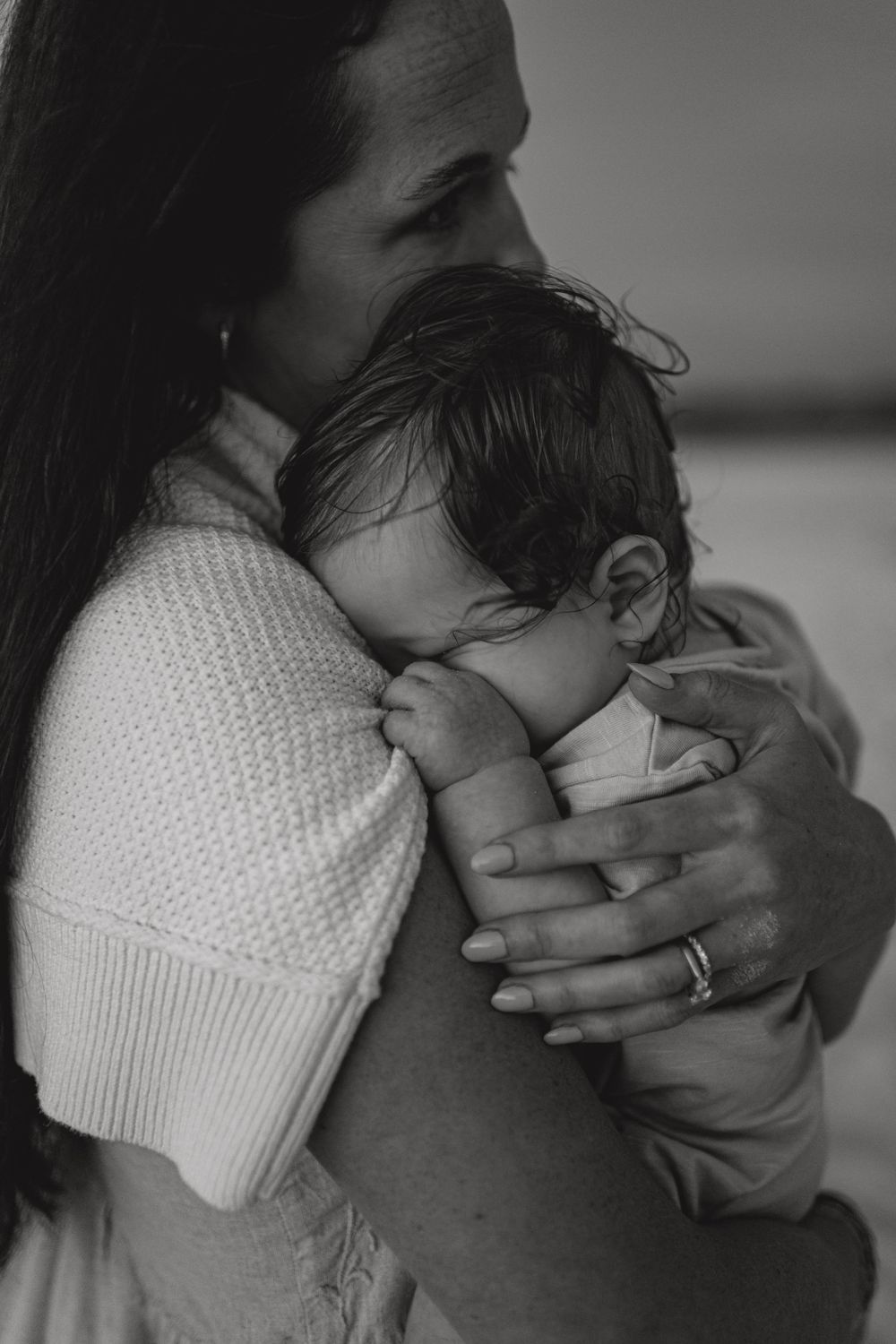 Black and white photo of a mother tenderly holding her newborn baby close to her chest, wearing a knit sweater.