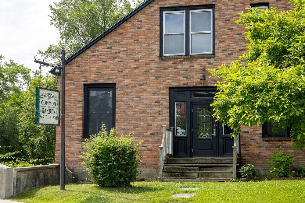 Classic brick commercial building with black double doors, business signage, and lush green trees in summer.