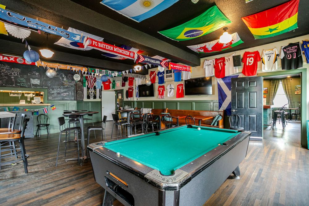 Sports bar featuring a pool table, international soccer flags, jerseys on walls, and dark wood floors.
