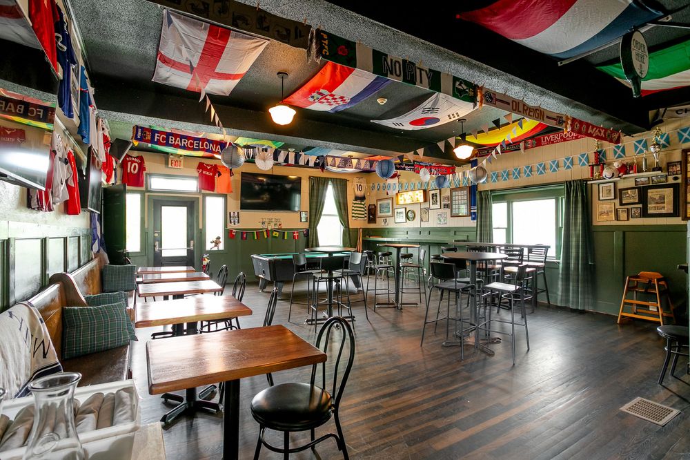 Cozy sports bar dining area with wooden tables, international flags hanging from ceiling, and green walls.