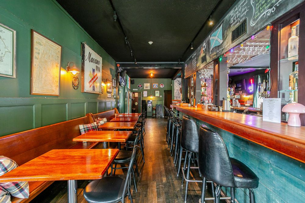 Narrow pub dining area with wooden tables, black bar stools, green wainscoting, chalkboard wall, and warm lighting.