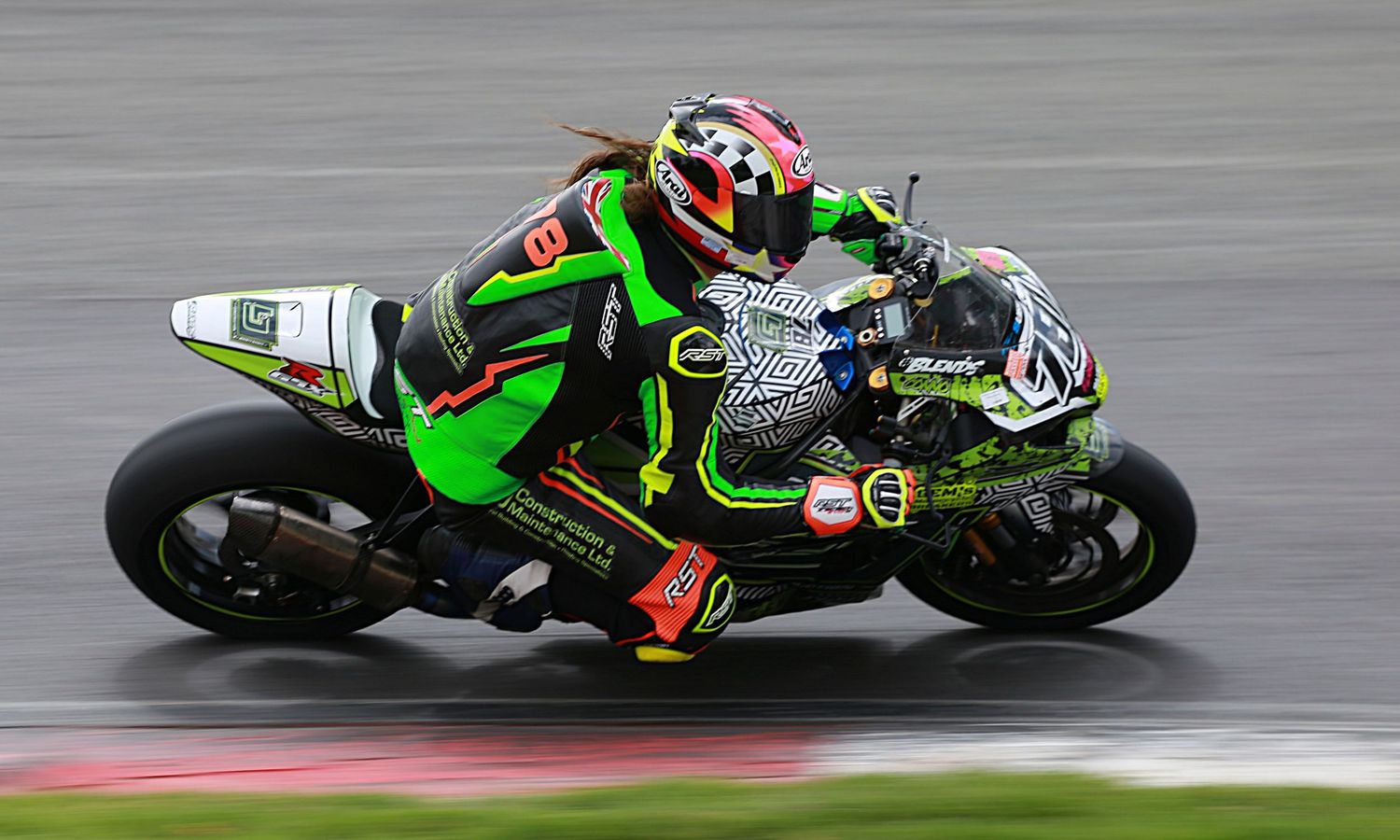 Green Kawasaki superbike racer leaning aggressively into a wet corner at a professional motorcycle race.