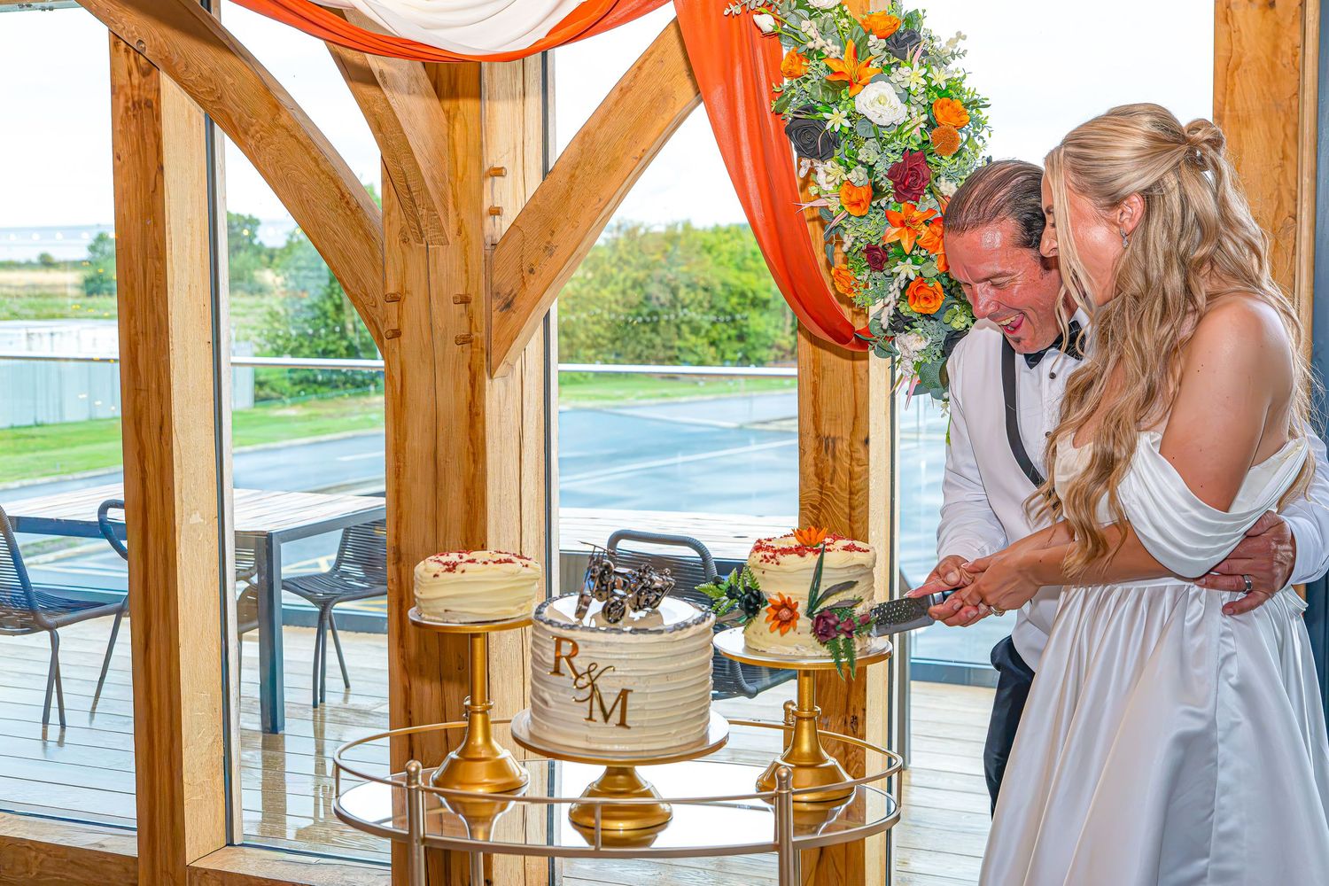 Bride and groom cutting their wedding cake decorated with R&M monogram inside a rustic wooden venue.Yorkshire, Sheffield, Lincolnshire, UK