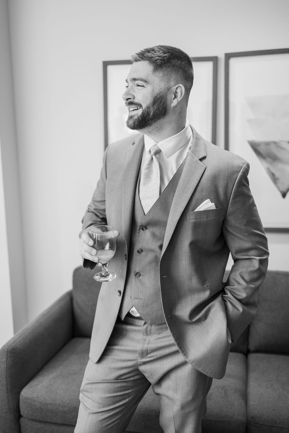 A well-dressed man in a three-piece suit holds a wine glass while smiling in a black and white portrait photo.