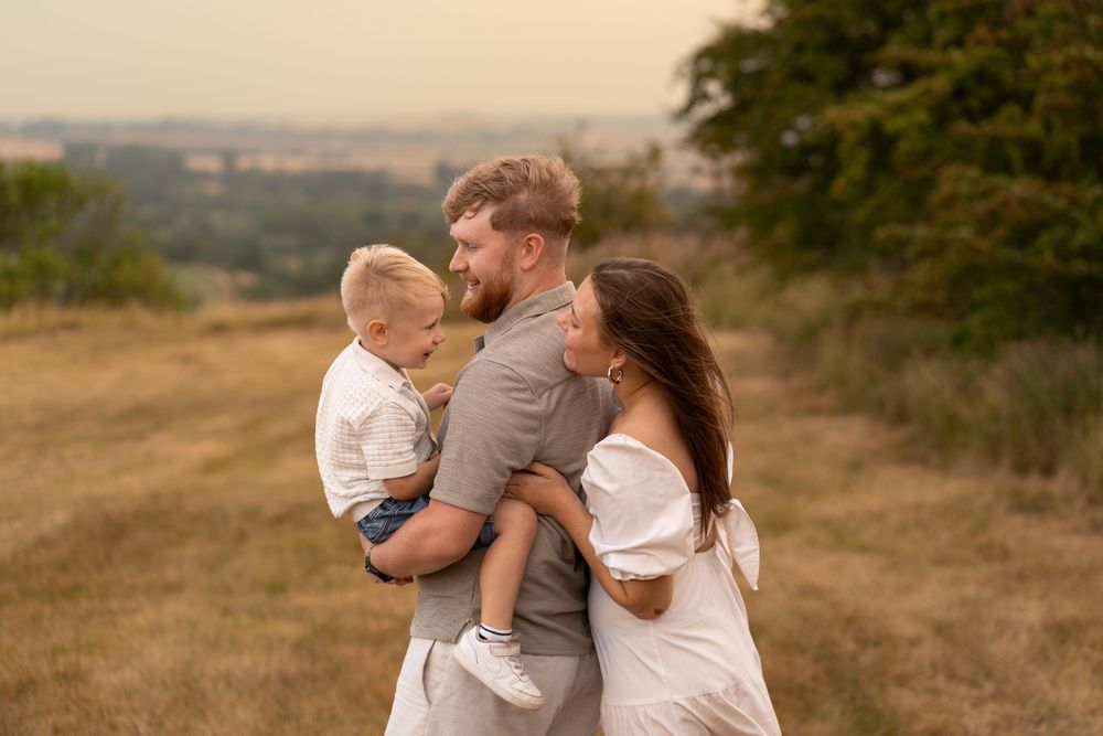 A happy young family with a toddler embracing outdoors in a golden field at sunset.