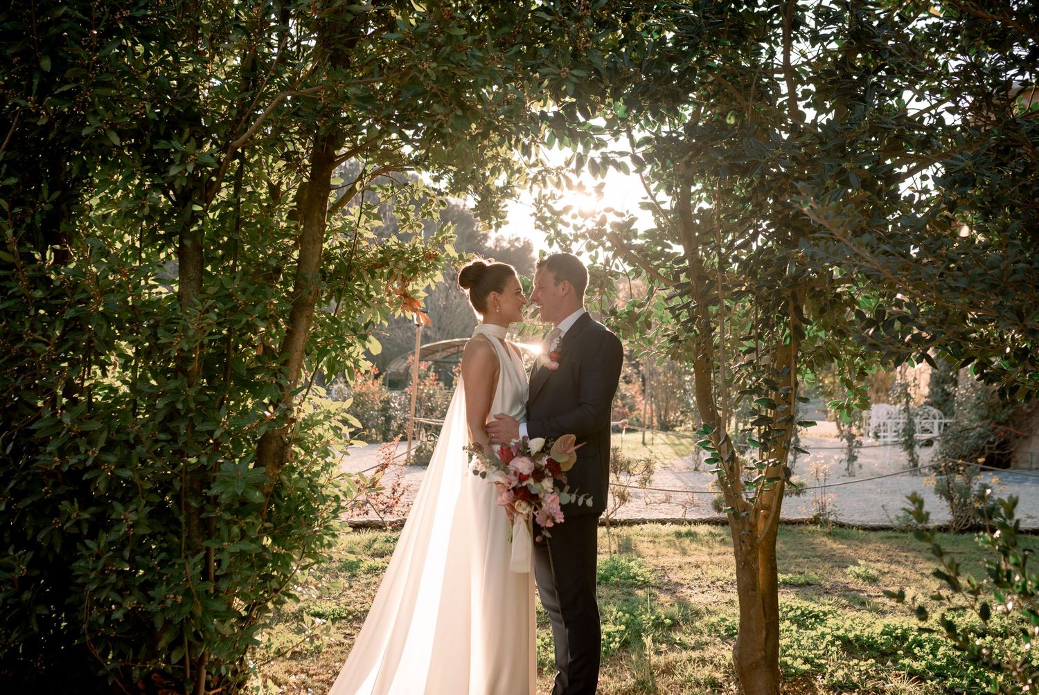 Bride and groom sharing a romantic moment under a natural tree arch with a colorful bridal bouquet at Borgo di Tragliata.