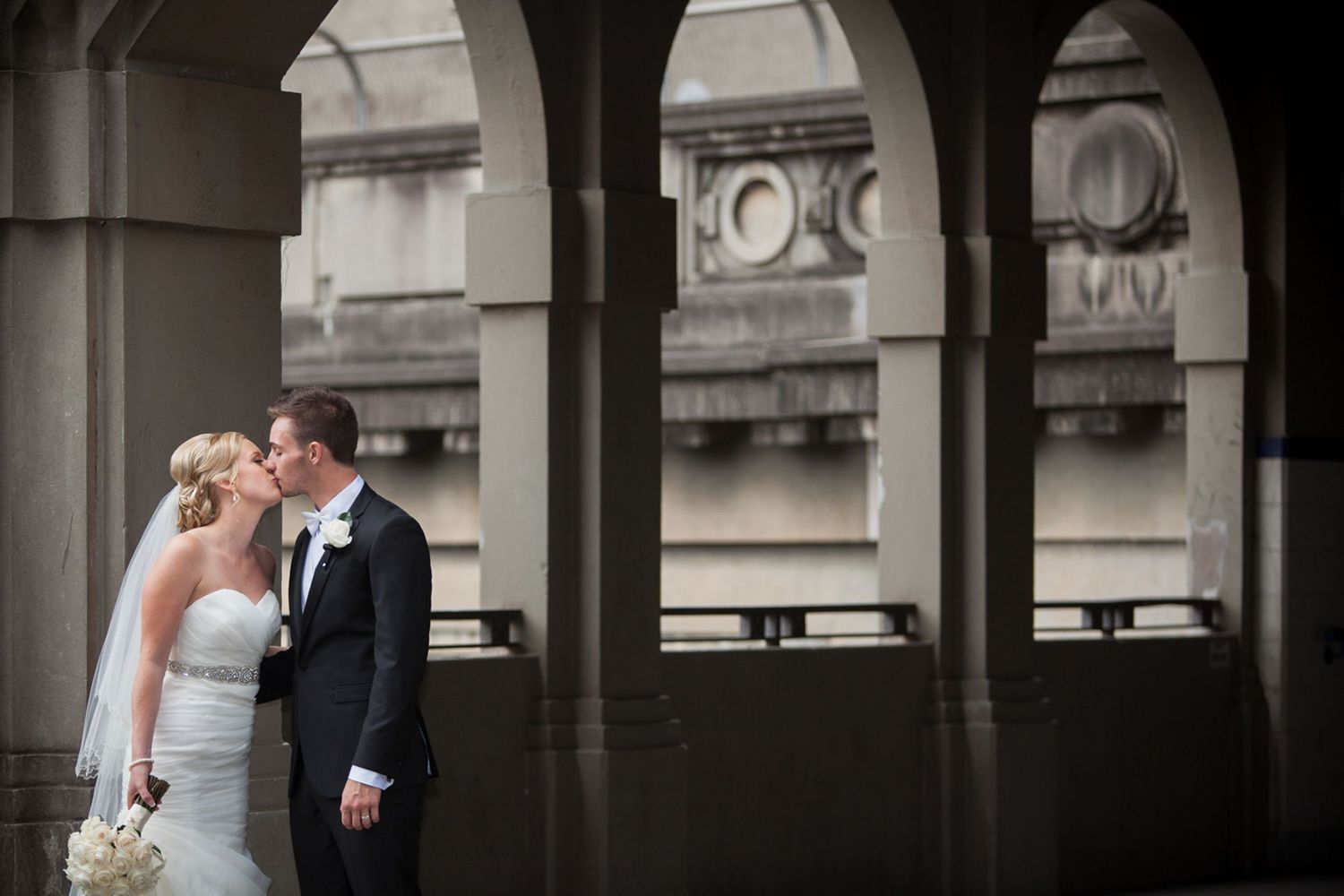 Bride and groom kissing under stone arches, captured for romantic wedding photos by a Suffolk wedding photographer.