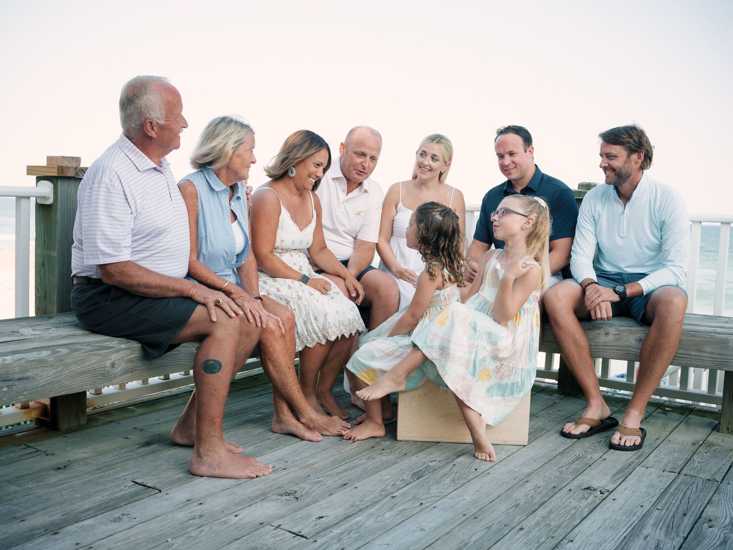 Multi-generational family group smiling together on a wooden beach deck during a casual outdoor portrait session.