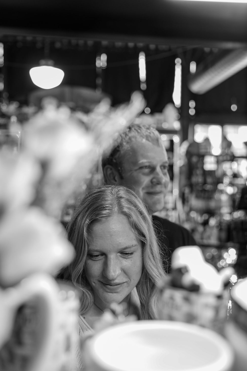Black and white photo of a smiling couple at a restaurant bar, woman with blonde hair in foreground.
