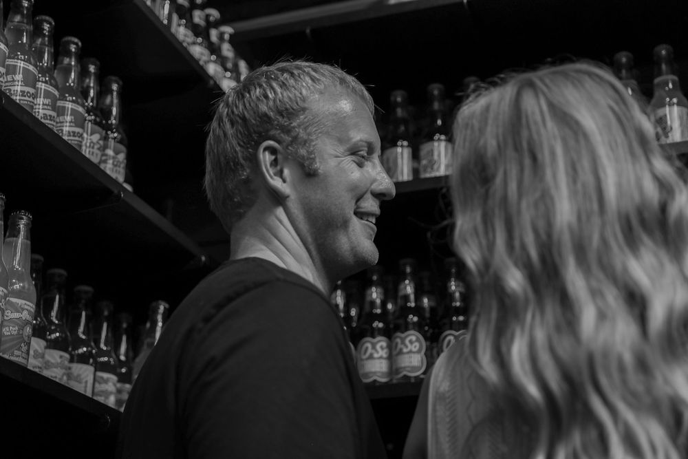 Black and white photo of a couple sharing a romantic moment in front of shelves of beer bottles.