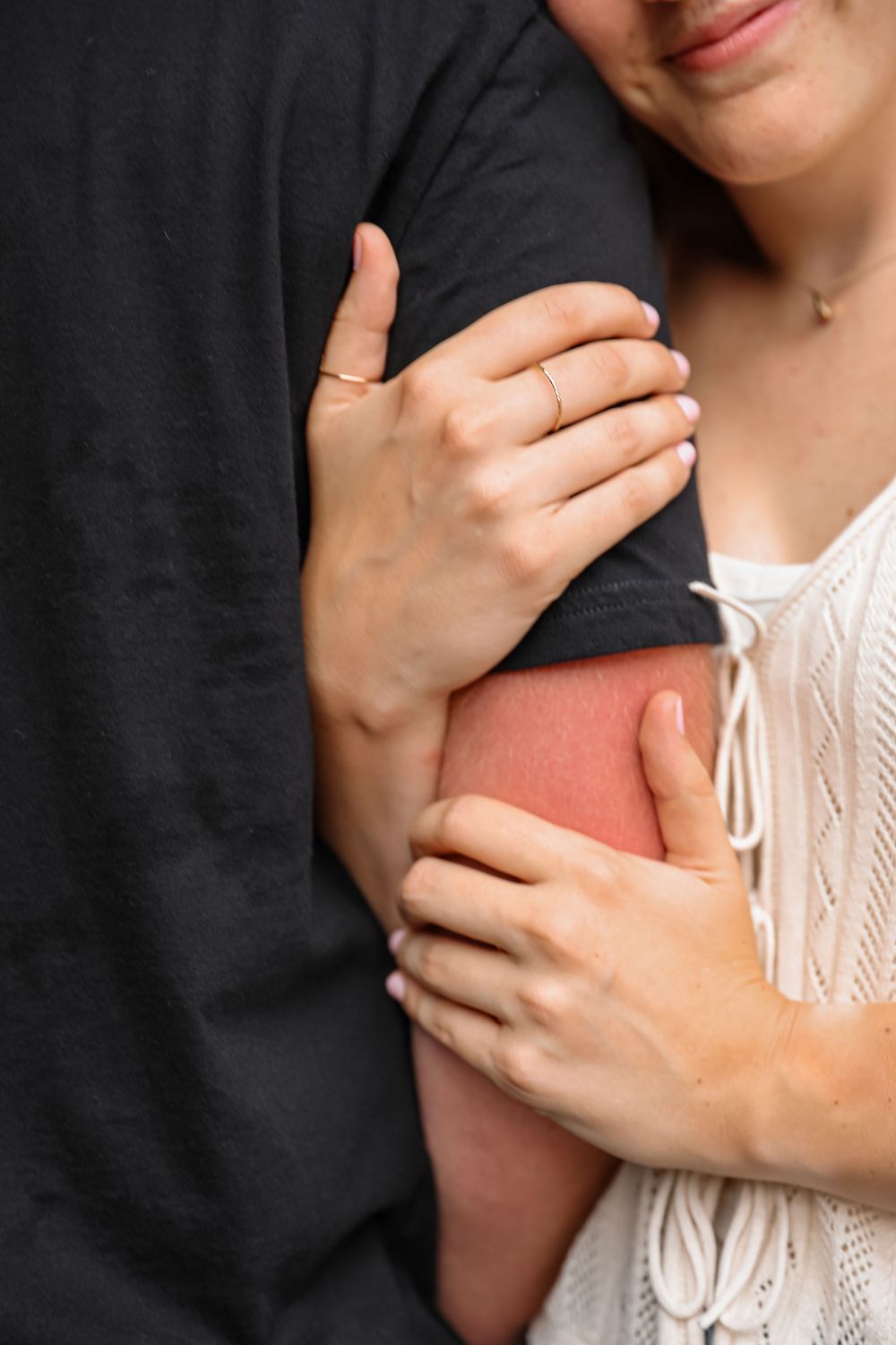 Close-up of a couple embracing, woman wearing a ring holds mans arm in a tender romantic moment.
