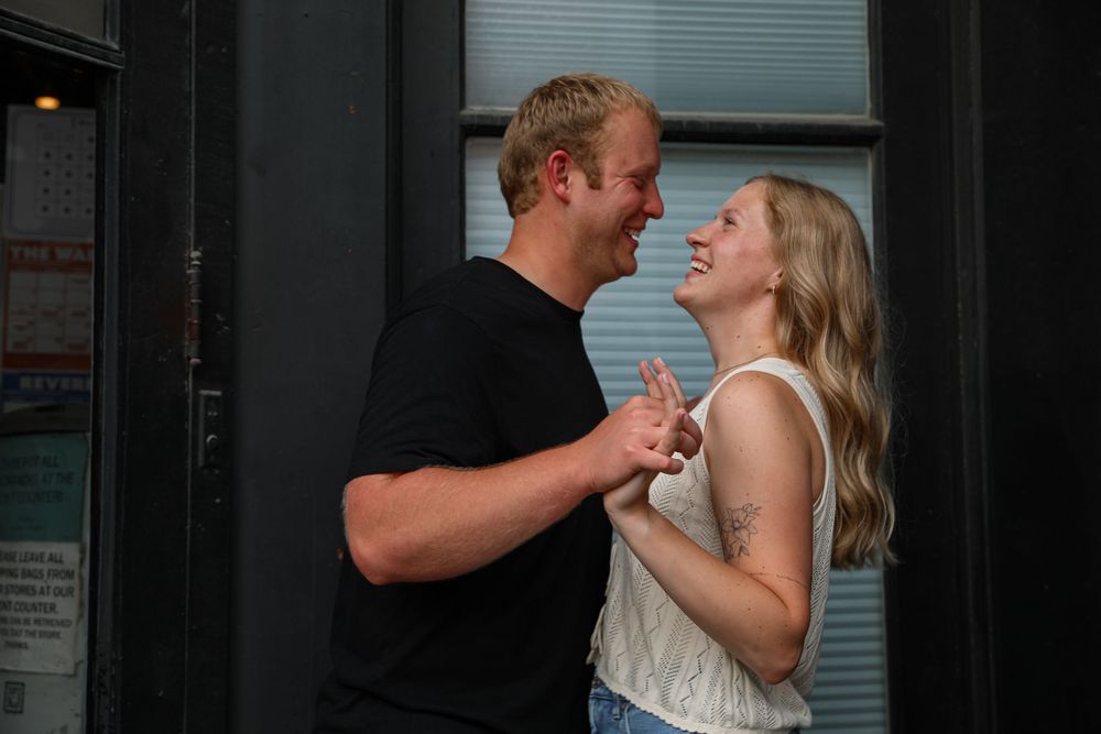 Joyful couple holding hands and laughing together outside a building entrance.
