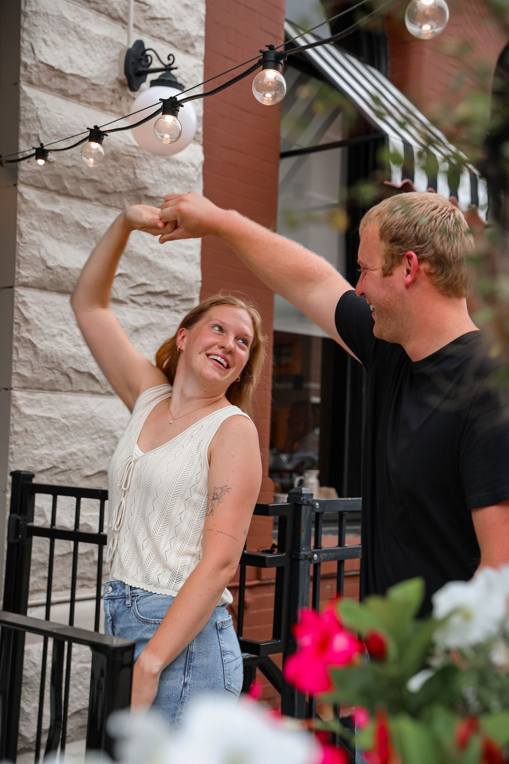 Happy couple dancing outdoors on a patio, man spinning smiling woman under string lights.