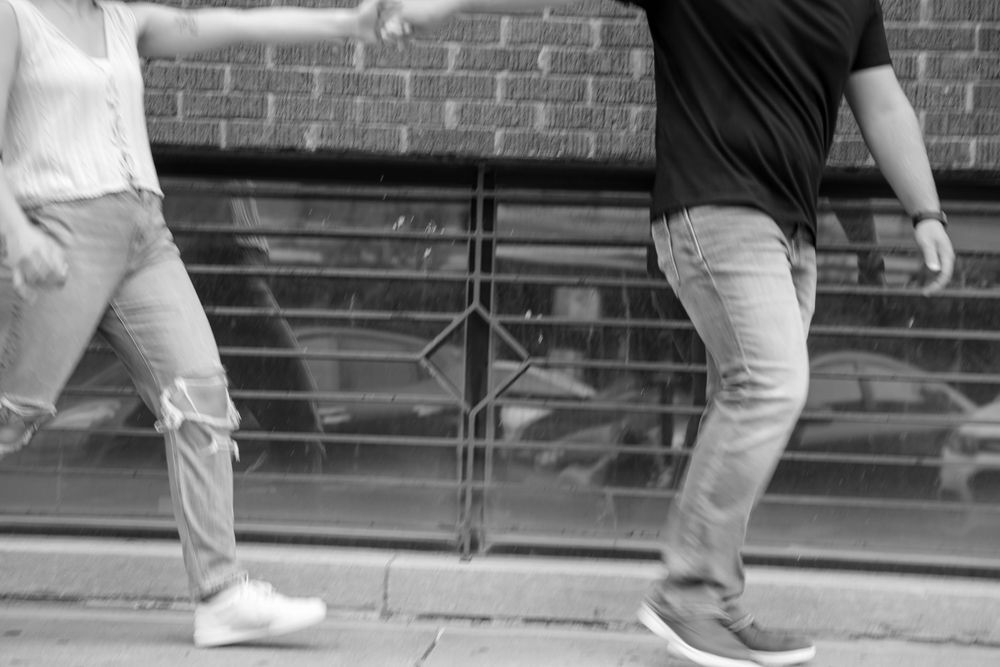 Black and white photo of two people holding hands while walking on a sidewalk near a brick building.