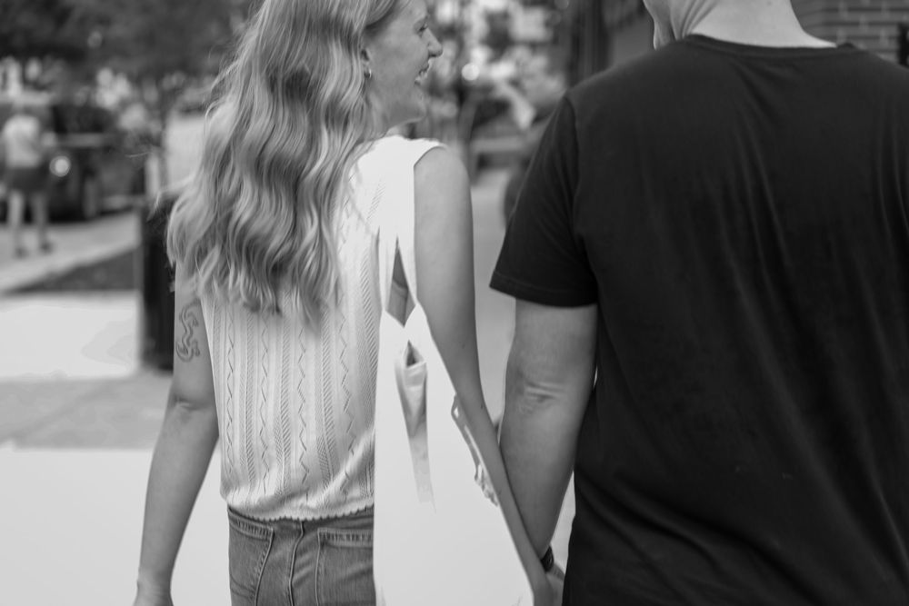 Black and white photo of a couple holding hands while walking outdoors on a sunny day.