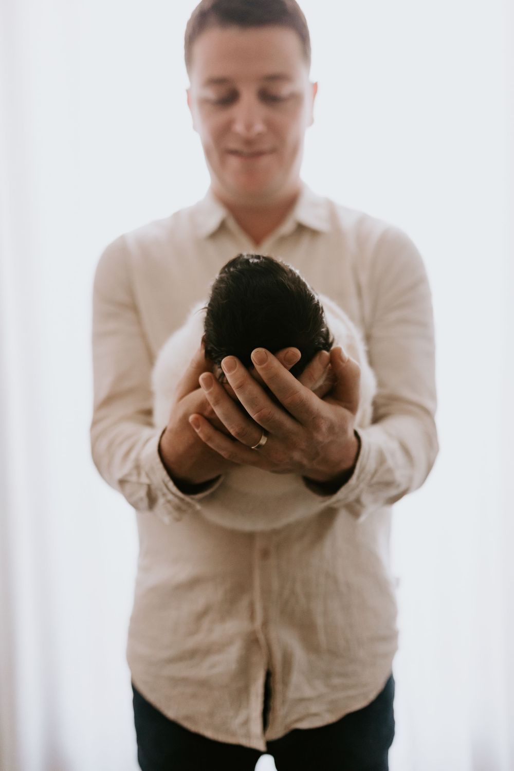 Man in beige linen shirt gently holding a ripe avocado with both hands indoors.