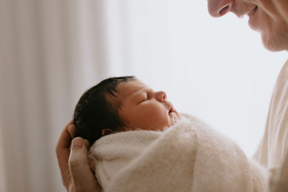Newborn baby sleeping peacefully wrapped in a soft blanket while being held by a parent.