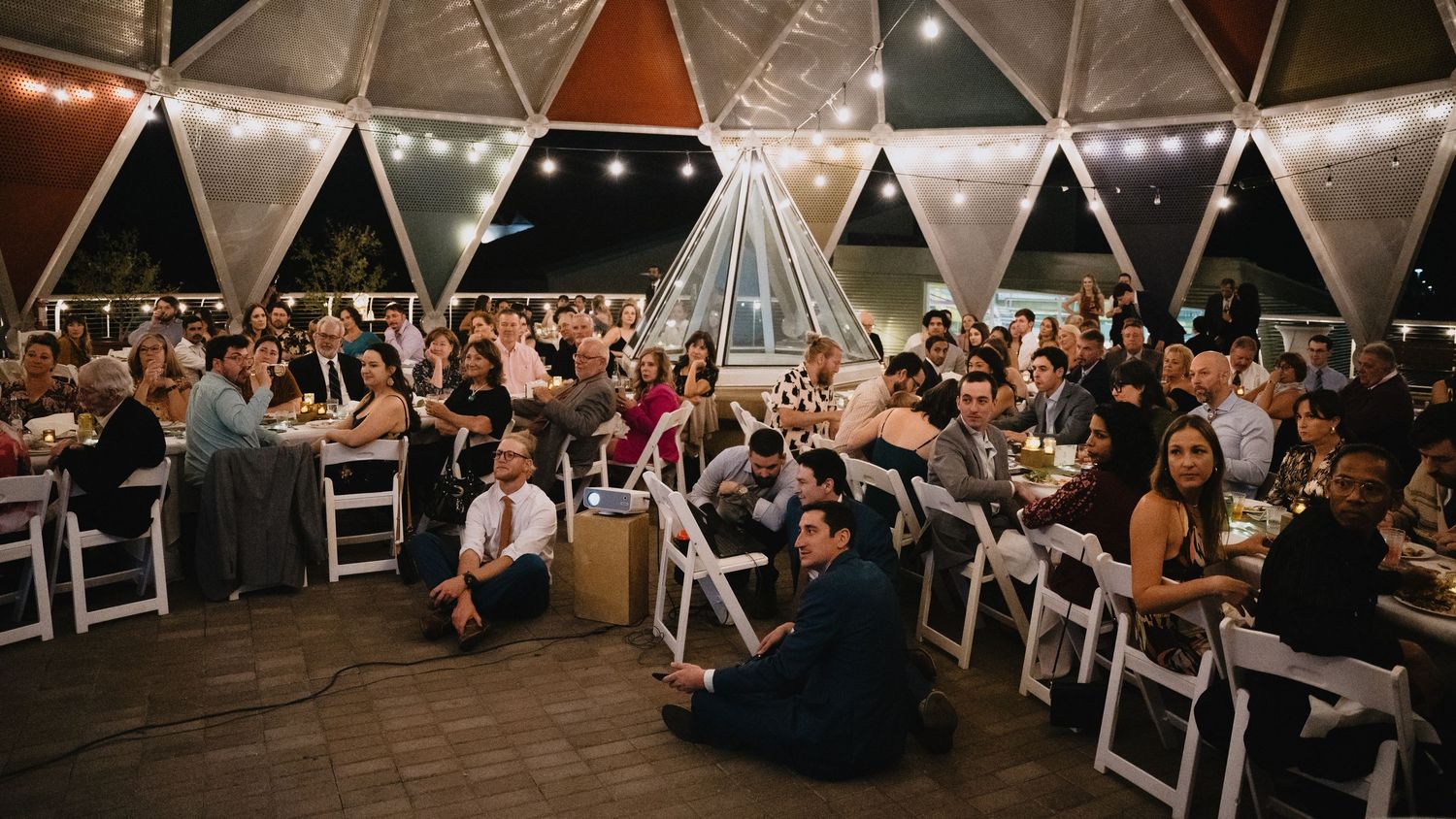 Elegant outdoor wedding reception under a geometric dome tent with guests seated at decorated tables illuminated by string lights at night.