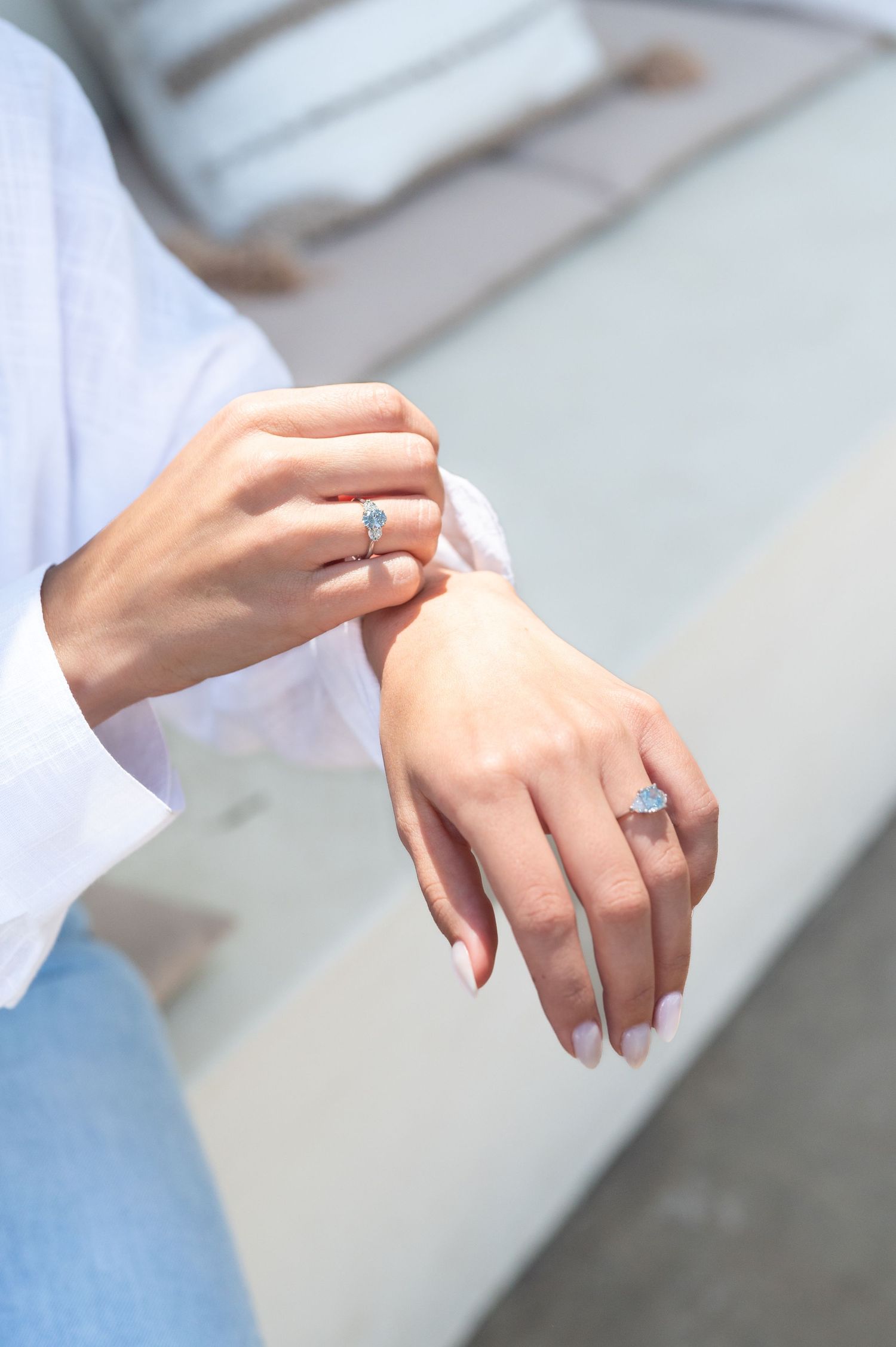 Close-up view of hands wearing a delicate silver ring against a soft white and blue background.