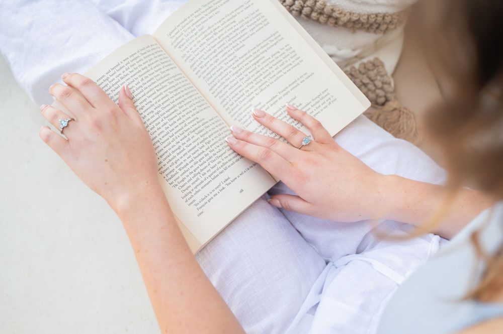 Woman reading an open book, viewed from above, wearing rings on her fingers.