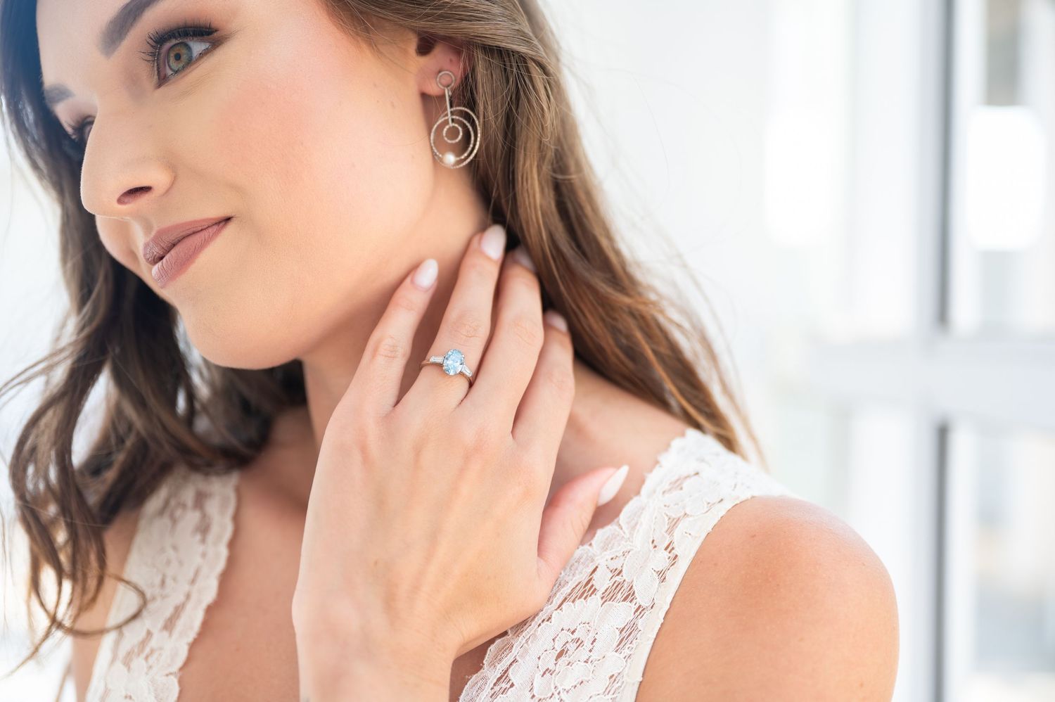 Close-up view of a woman wearing a white lace dress and delicate jewellery showing off her ring.