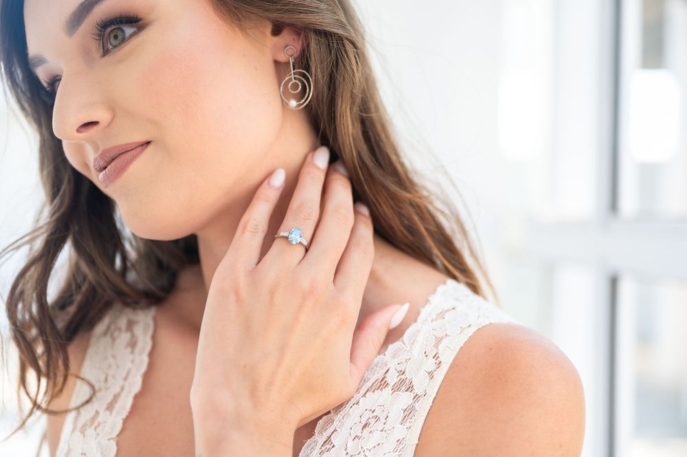 Close-up view of a woman wearing a white lace dress and delicate jewellery showing off her ring.