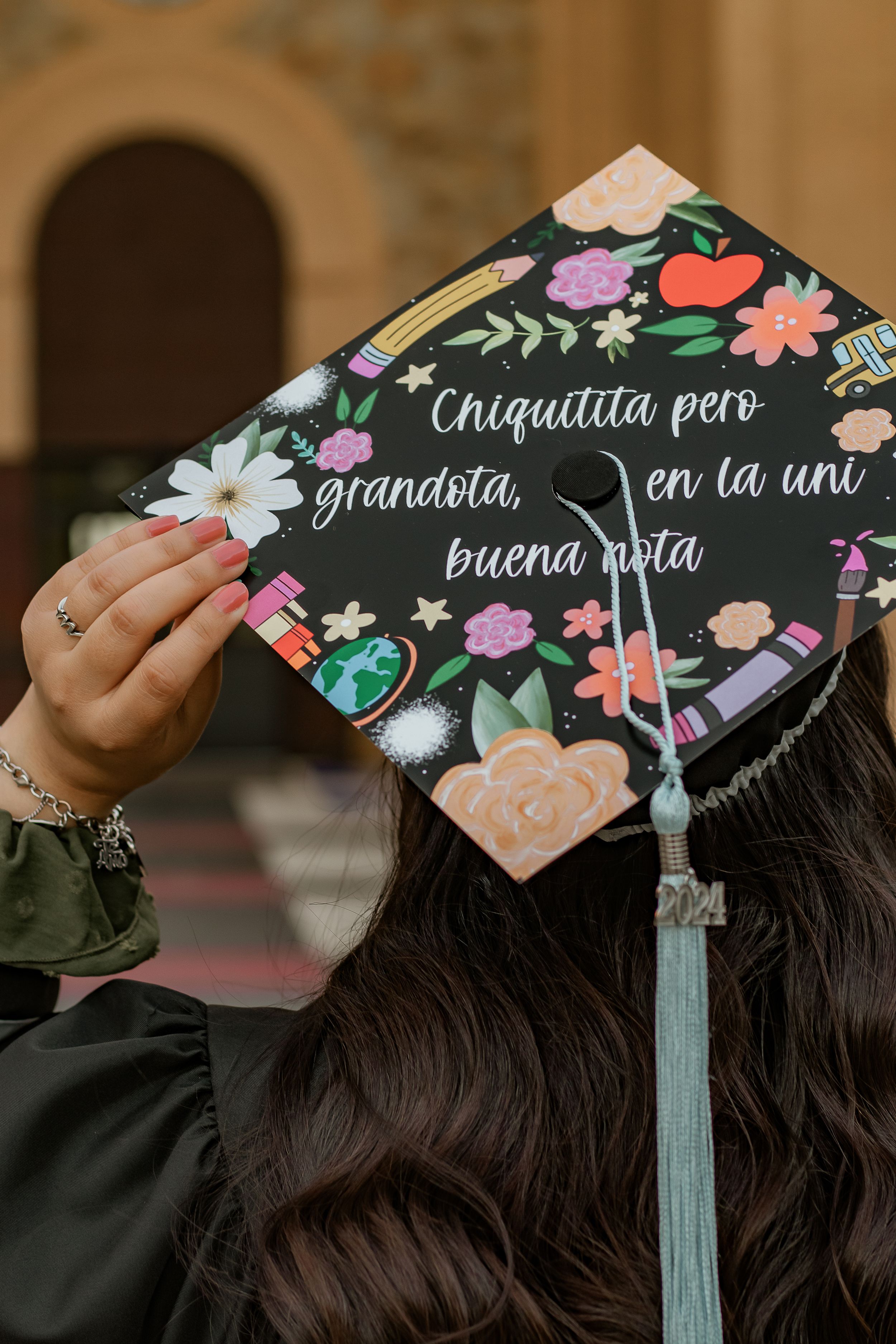 Decorated graduation cap with floral design and Spanish text reading Chiquititta pero grandota en la uni buena nota.