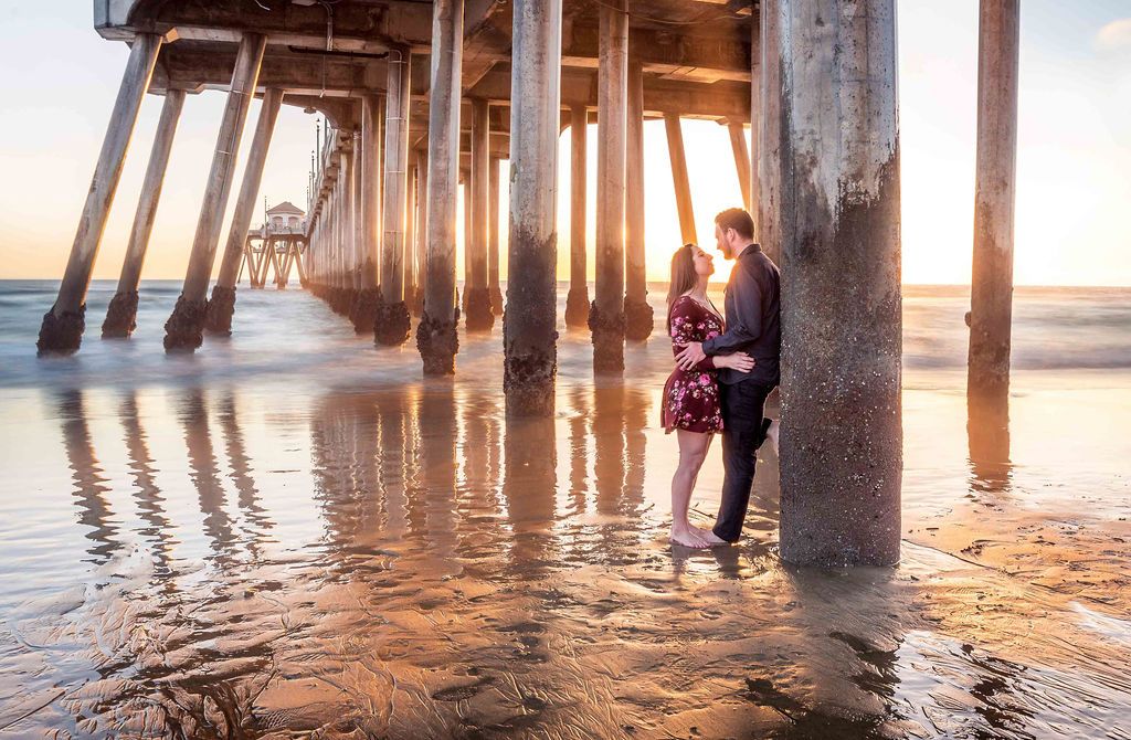 a couple in love embraces below the huntington beach pier during golden hour and low tide