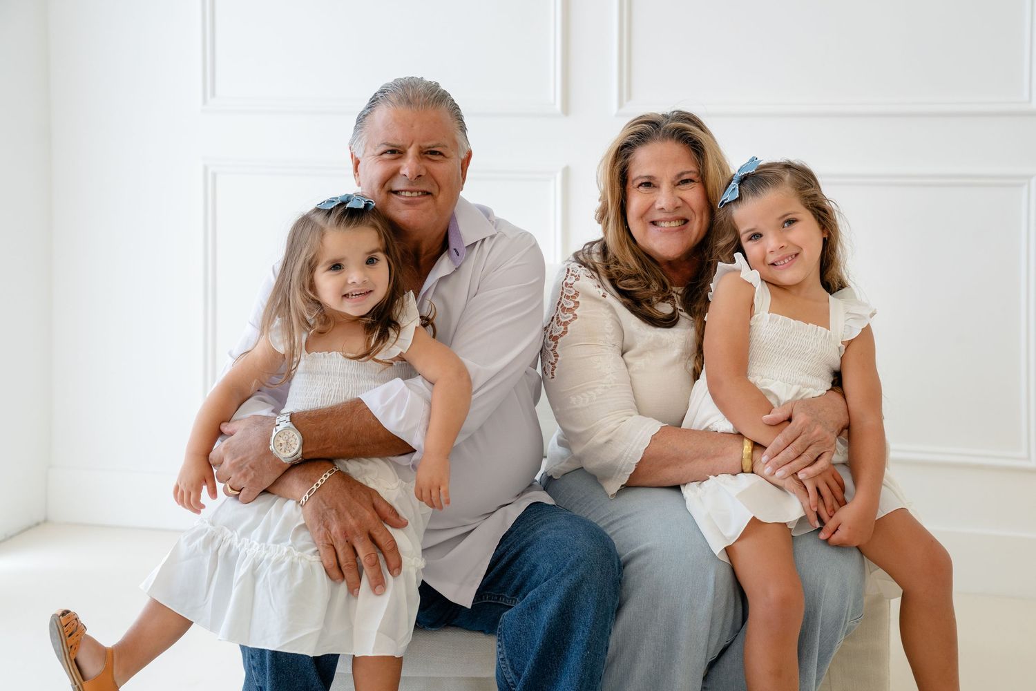 Grandparents smiling with two young girls in white dresses during a bright family portrait session.