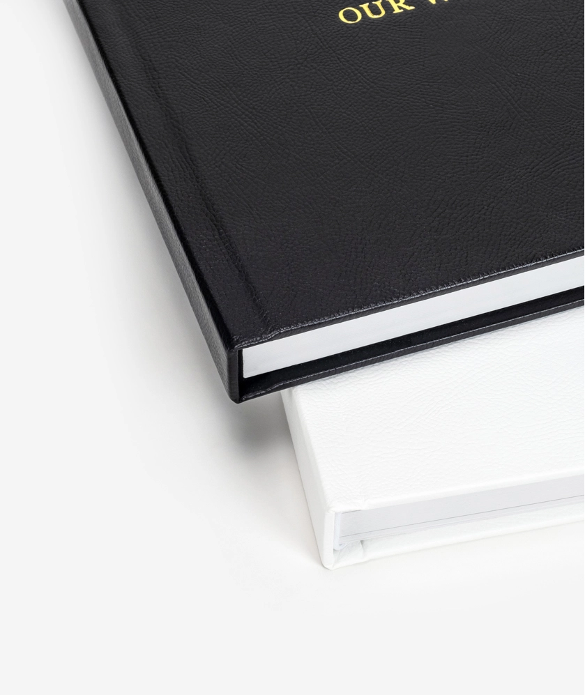 Corner of black hardcover book with gold lettering next to white book.