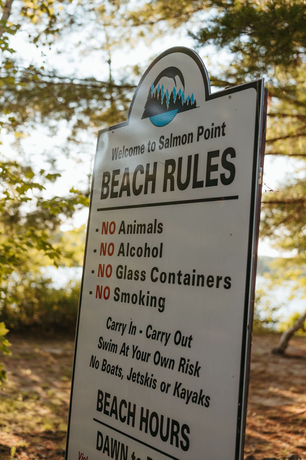 Salmon Point Beach Rules sign listing no animals, alcohol, glass, or smoking, with beach hours posted outdoors.