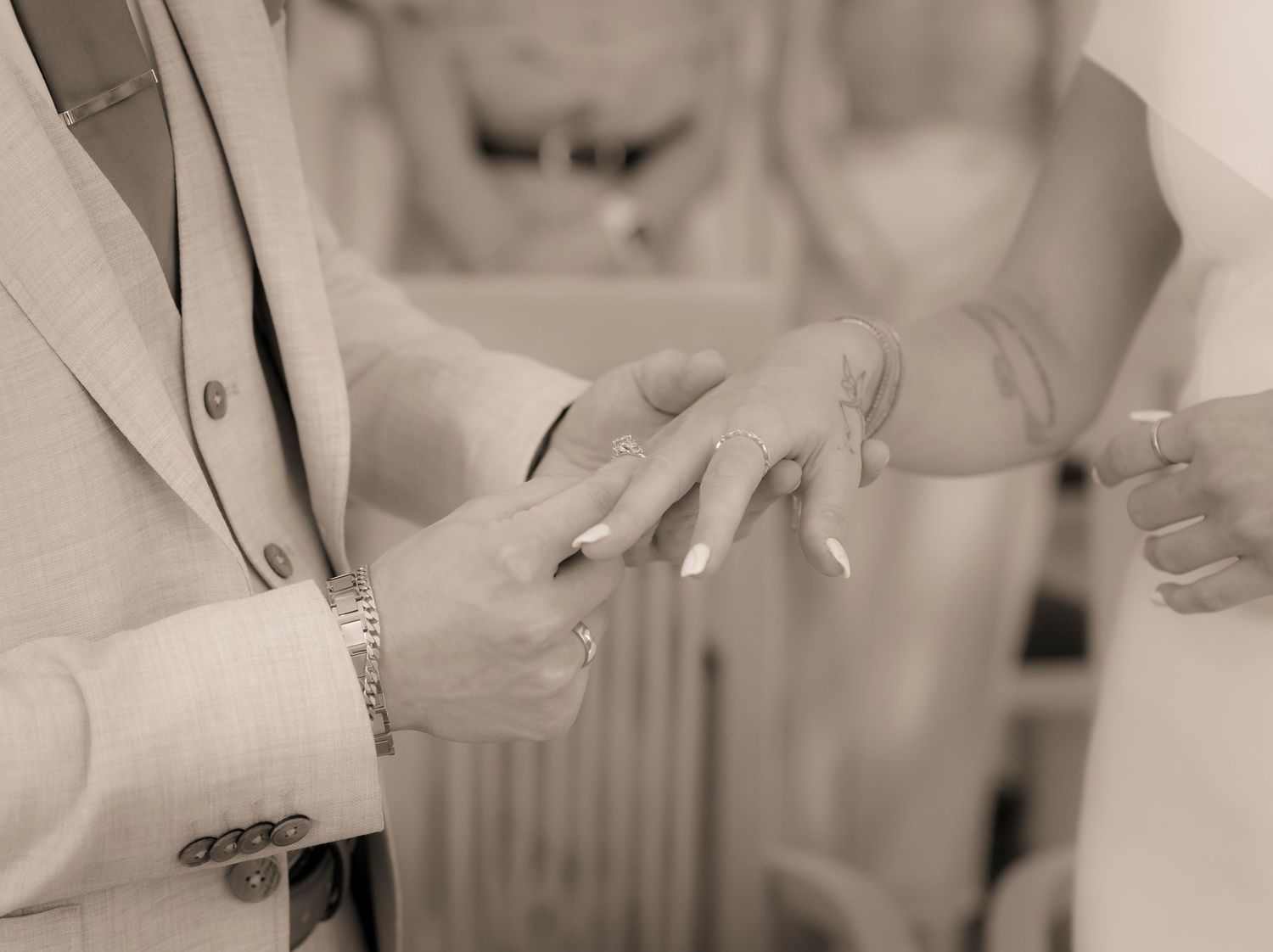 Groom placing wedding ring on bride's finger during ceremony in sepia tone.