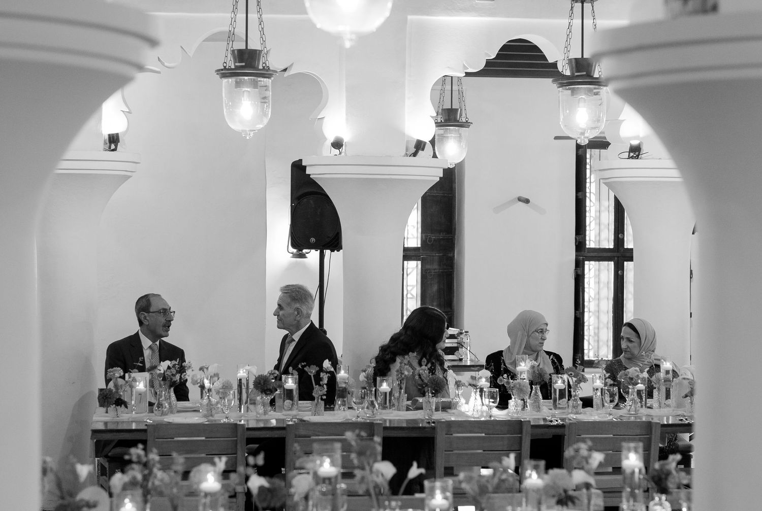 Black and white photo of elegantly dressed guests seated at a long banquet table in a grand reception hall.