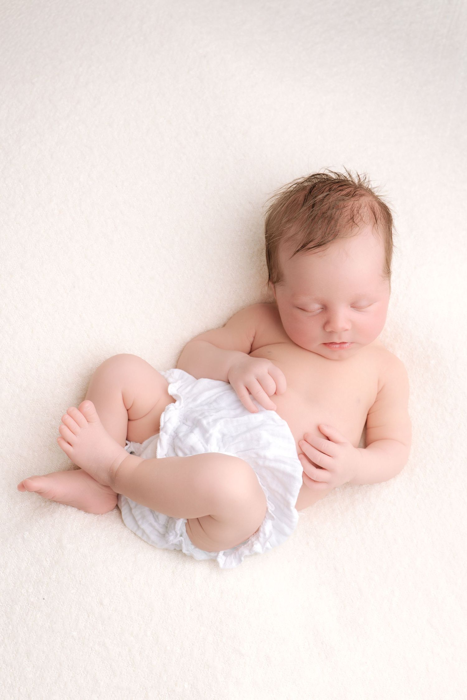 Black and white photo of a pregnant woman cradling her bare baby bump, wearing a cozy crop top and open cardigan.