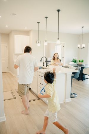 Family gathering in modern kitchen with white cabinets, pendant lights, and hardwood floors as mother holds baby.