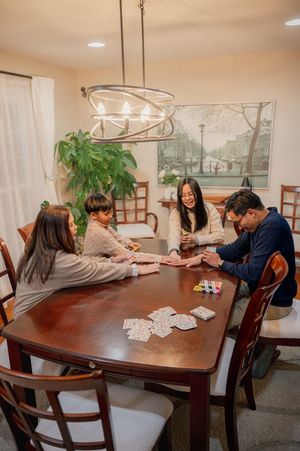 Family of four playing card games at a wooden dining table under a chandelier in a cozy home setting.