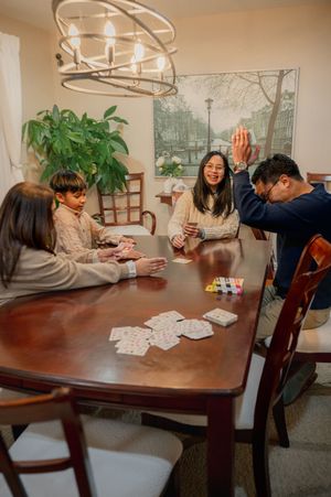 Family of four playing cards together at a wooden dining table, smiling and enjoying a fun game night at home.