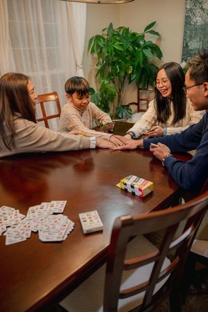 Family of four playing a card game together at a wooden dining table, smiling and enjoying game night at home.