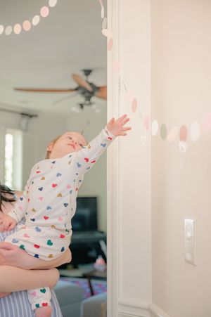 Baby in heart-print onesie reaching up toward pastel circle garland while being held by parent near doorway.