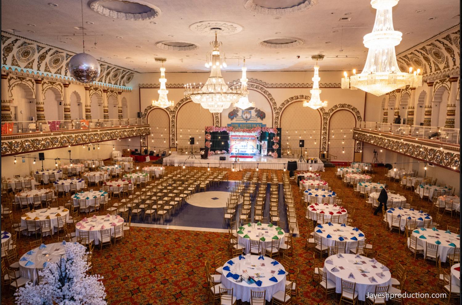 A grand ballroom with crystal chandeliers, round banquet tables, and a dance floor set for a large formal event.