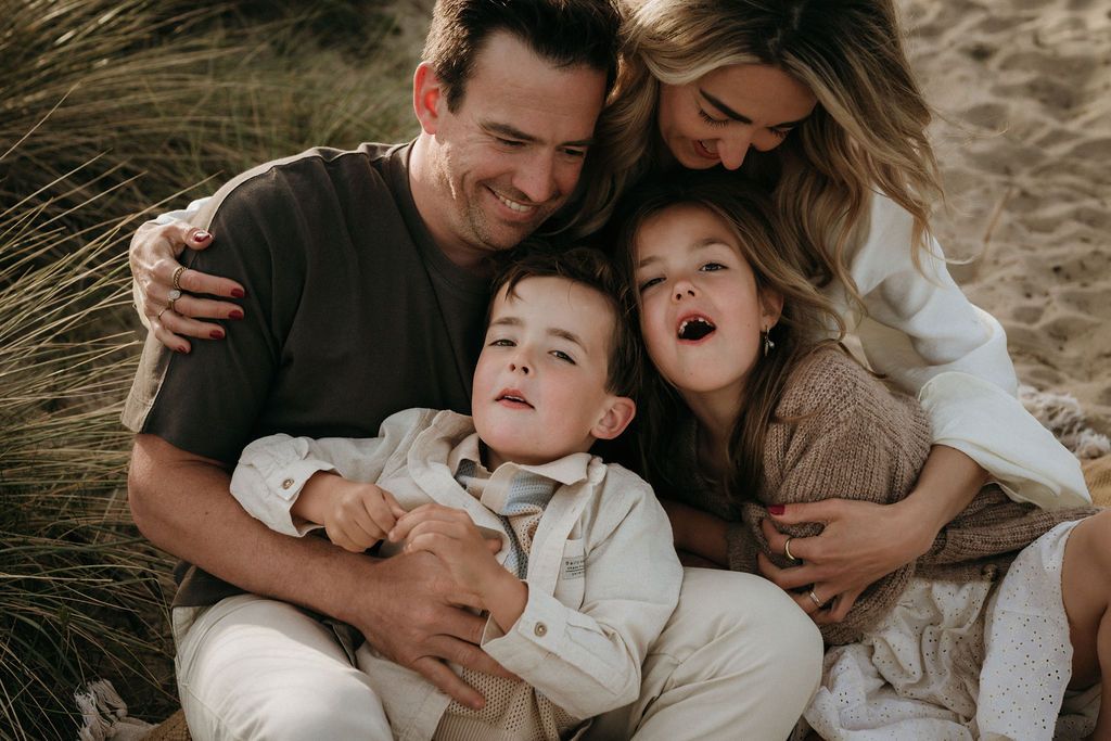 Gelukkig gezin hebben een fotoshoot aan zee, en knuffelen elkaar intiem, dichtbij Eindhoven.