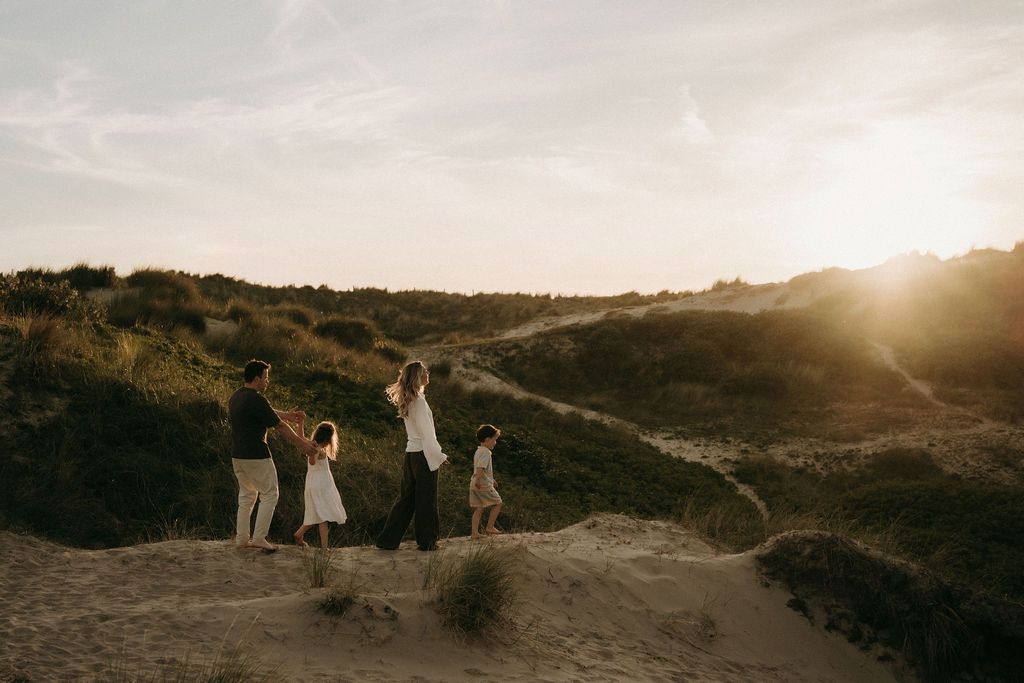Een familie van vier wandelen tijdens goldenhour met elkaar tijdens een fotoshoot aan zee, dichtbij Eindhoven.