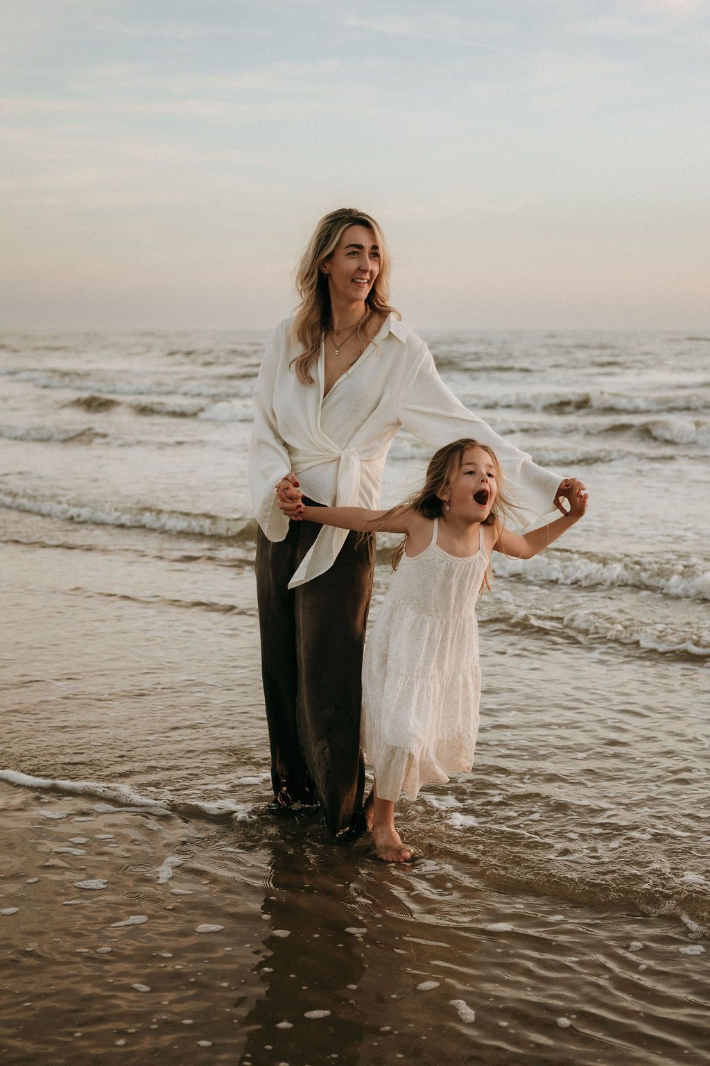 Een moeder en dochter dansen samen tijdens een serene zonsondergang, met een fotoshoot aan zee, dicht in de buurt van Eindhoven.