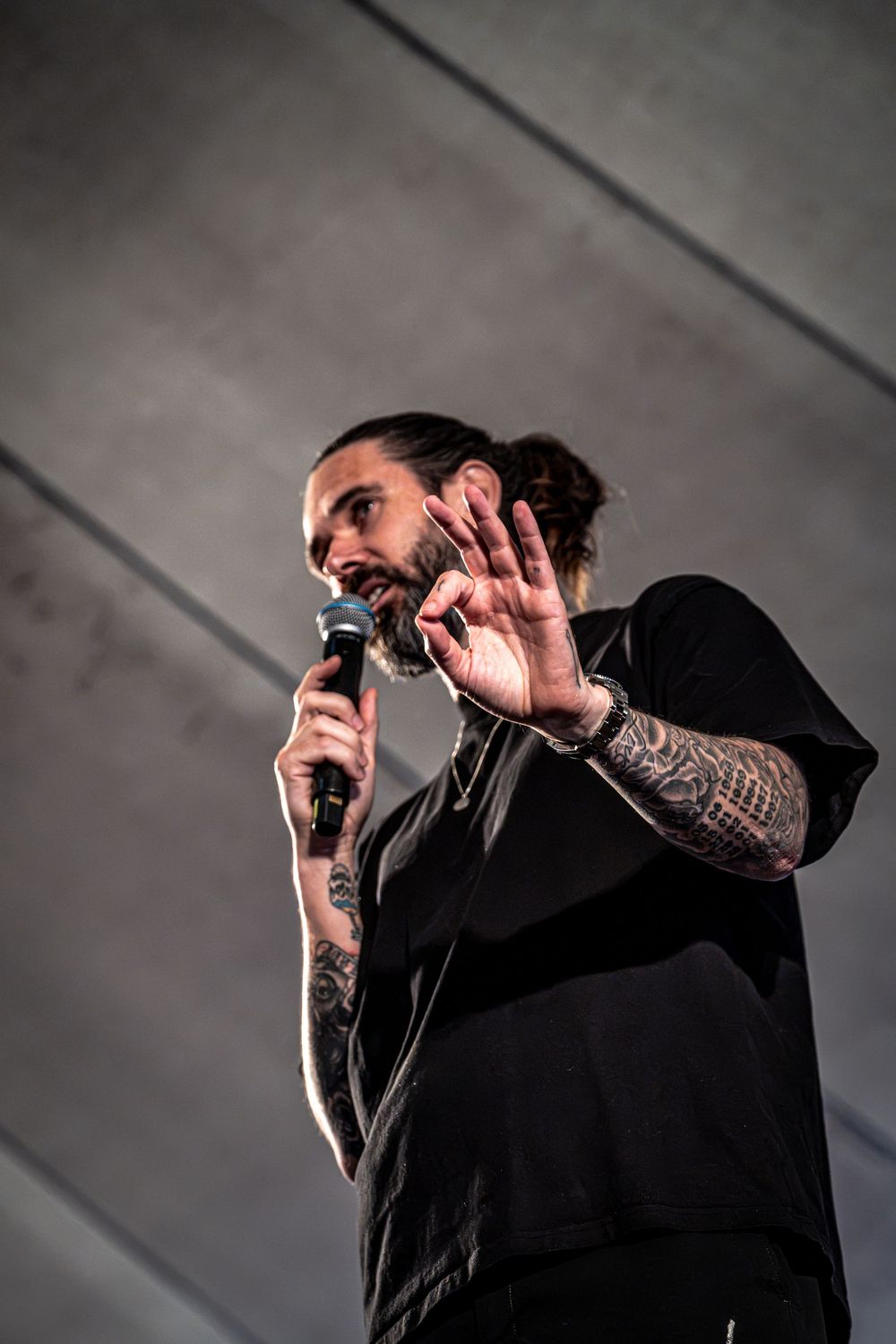 Bearded tattooed speaker holding microphone gesturing with hand while presenting on stage.