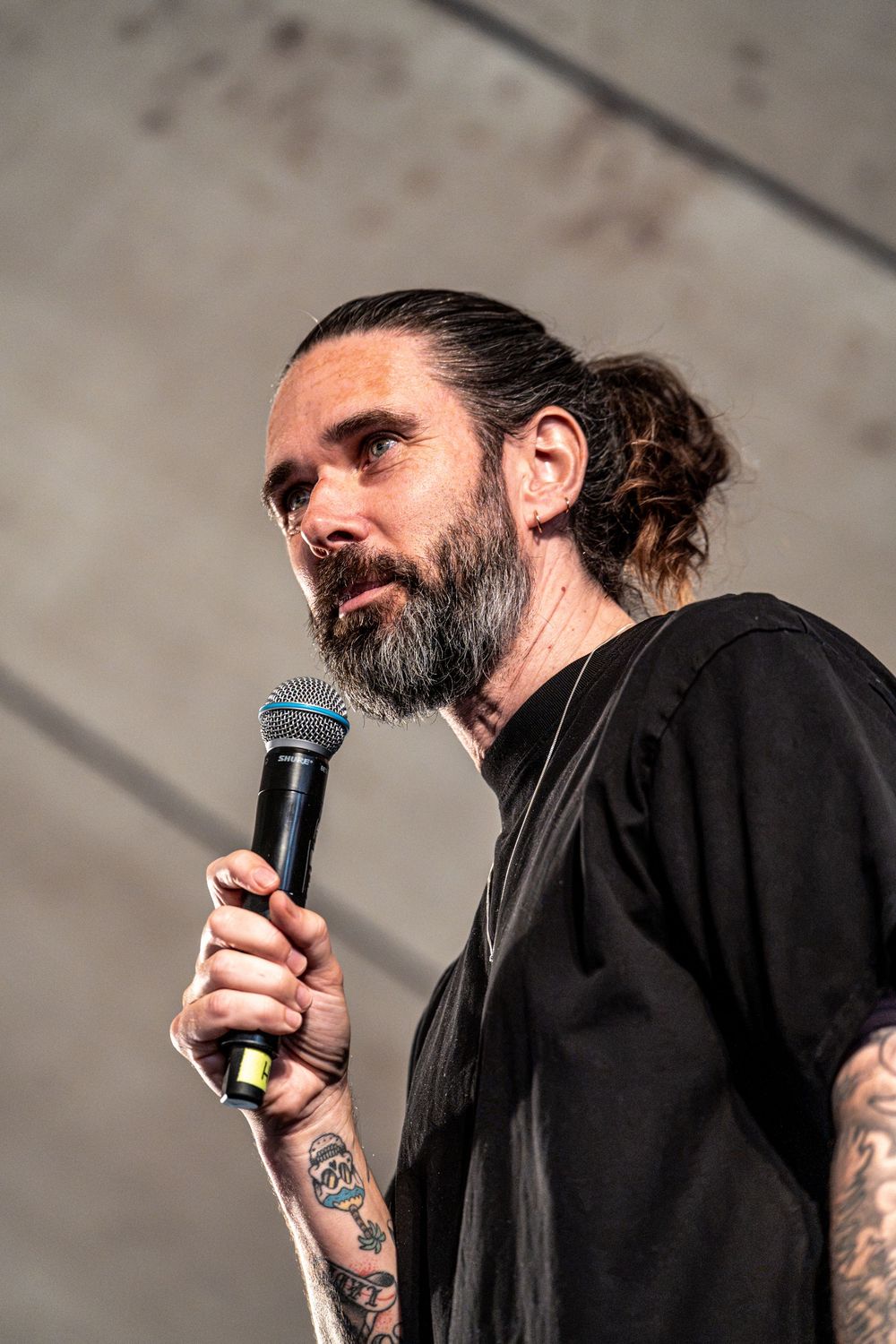 Close-up of bearded tattooed male vocalist performing on stage holding a microphone.