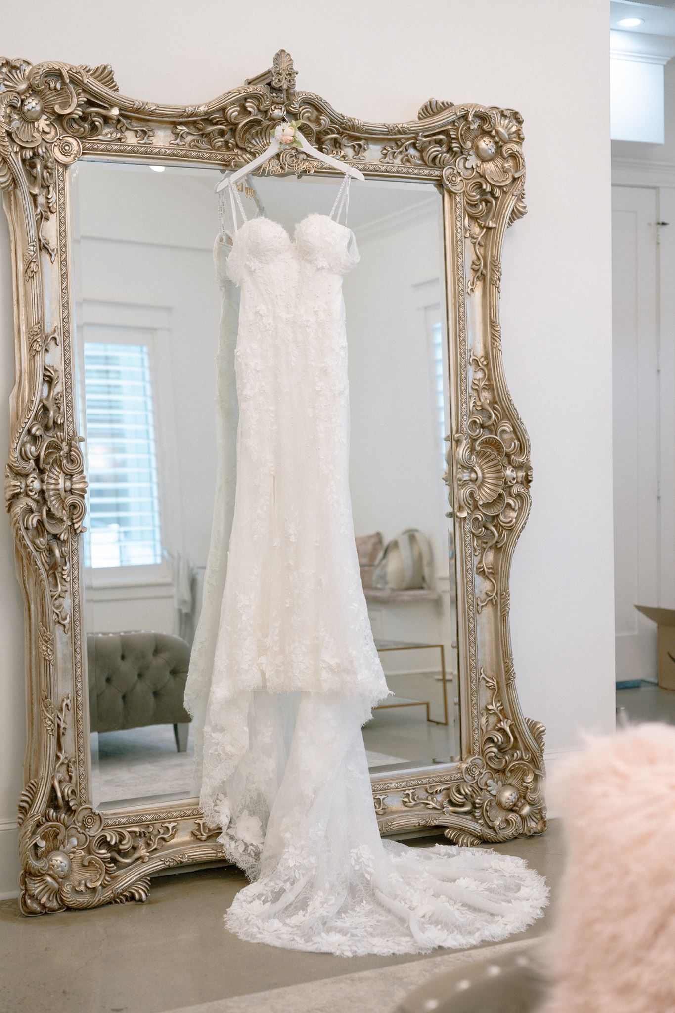 White lace wedding dress hanging on ornate gold mirror in elegant bridal suite.