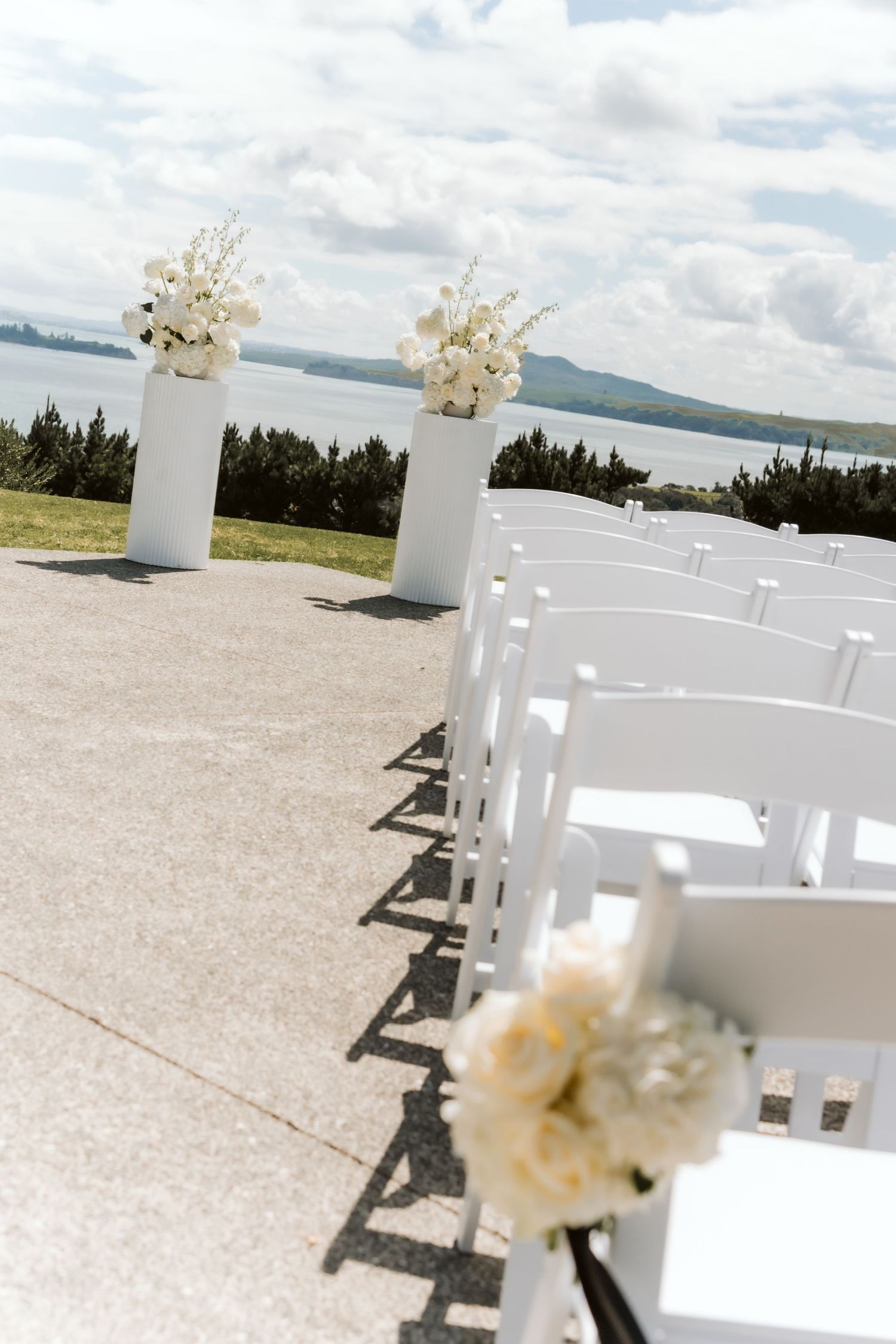 White roses and blue hydrangeas arranged in white urns at an outdoor wedding ceremony with ocean views.