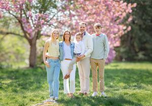 Family of six posing outdoors in spring park with blooming pink cherry blossom trees on green grass.