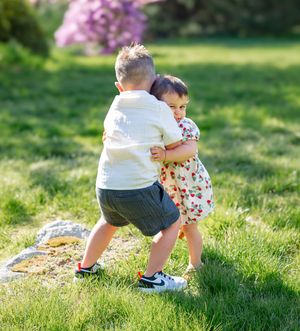 Two young children hugging and playing together on a sunny green grass lawn outdoors.
